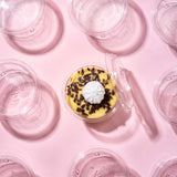 Coppetta per monoporzioni dall'alto, piena di dolce e aperta, tra tante coppette monoporzione chiuse e vuote, su sfondo rosa