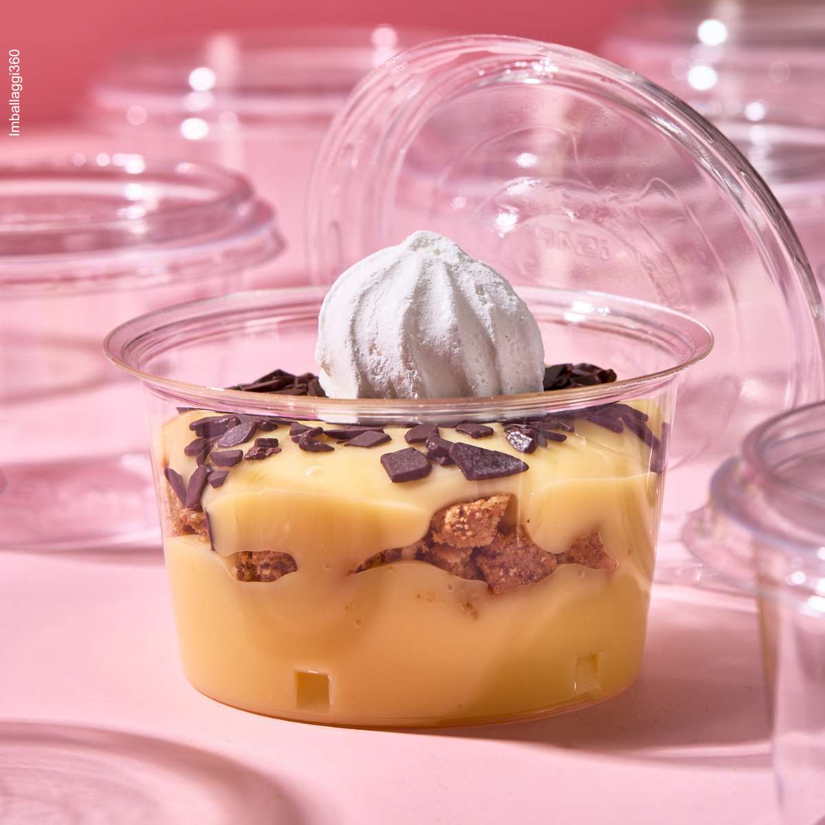 Coppetta in primo piano per monoporzioni, piena di dolce e aperta, tra tante coppette monoporzione chiuse e vuote, su sfondo rosa.