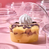 Coppetta in primo piano per monoporzioni, piena di dolce e aperta, tra tante coppette monoporzione chiuse e vuote, su sfondo rosa.