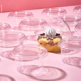 Coppetta per monoporzioni, piena di dolce e aperta, tra tante coppette monoporzione chiuse e vuote, su sfondo rosa