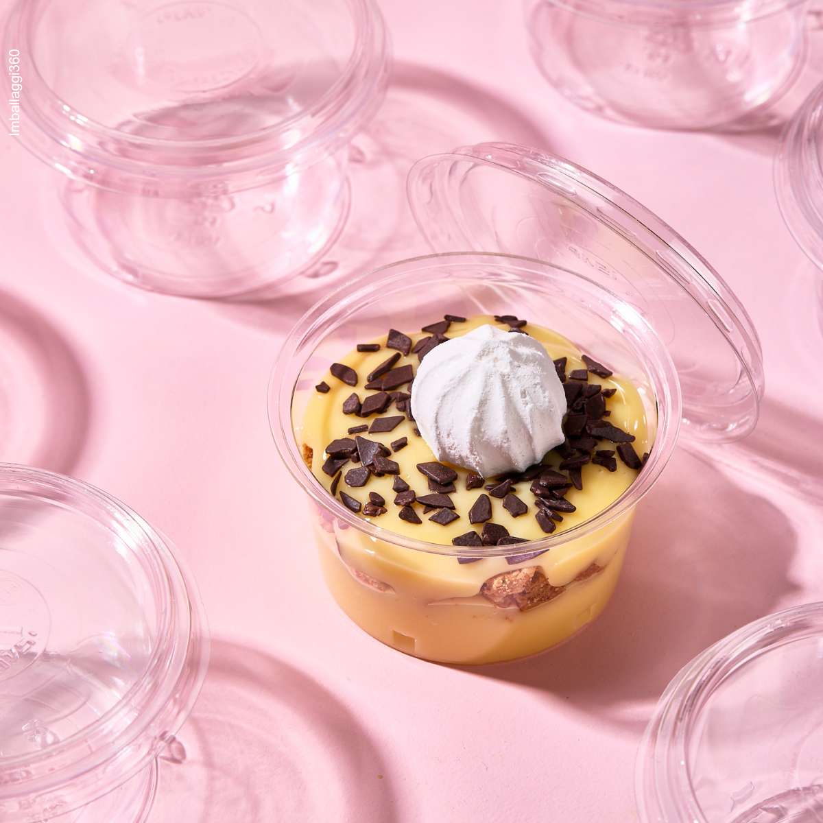 Coppetta per monoporzioni. dettaglio dall'alto, piena di dolce e aperta, tra tante coppette monoporzione chiuse e vuote, su sfondo rosa