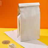 Sacchetto per farina, mostrato in piedi e pieno, su uno steso vuoto, accanto a farina e chicchi di grano