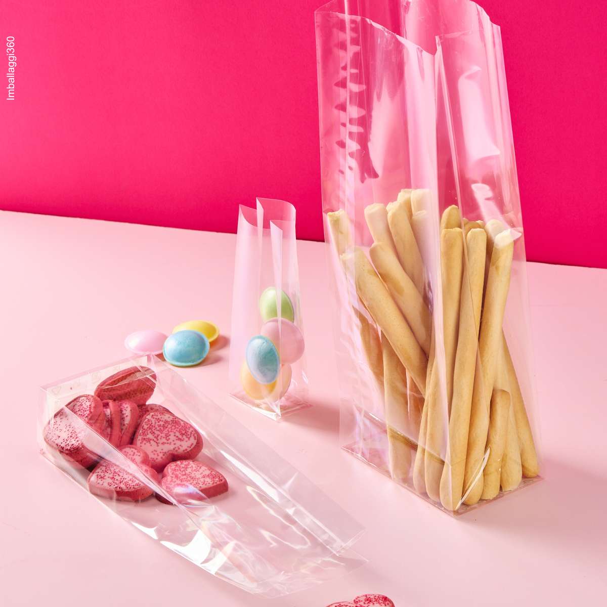 Sacchetto trasparenti a fondo quadro, ripieni di dolci e grissini, varie misure, su sfondo rosa
