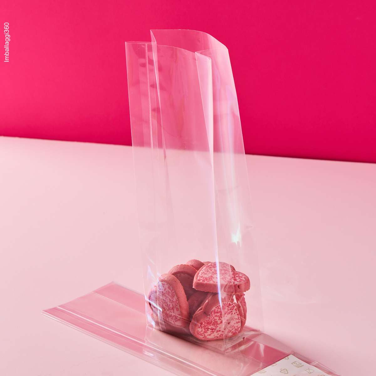 Sacchetto trasparente a fondo quadro, ripieni di dolci, su sfondo rosa, mostrato pieno e steso
