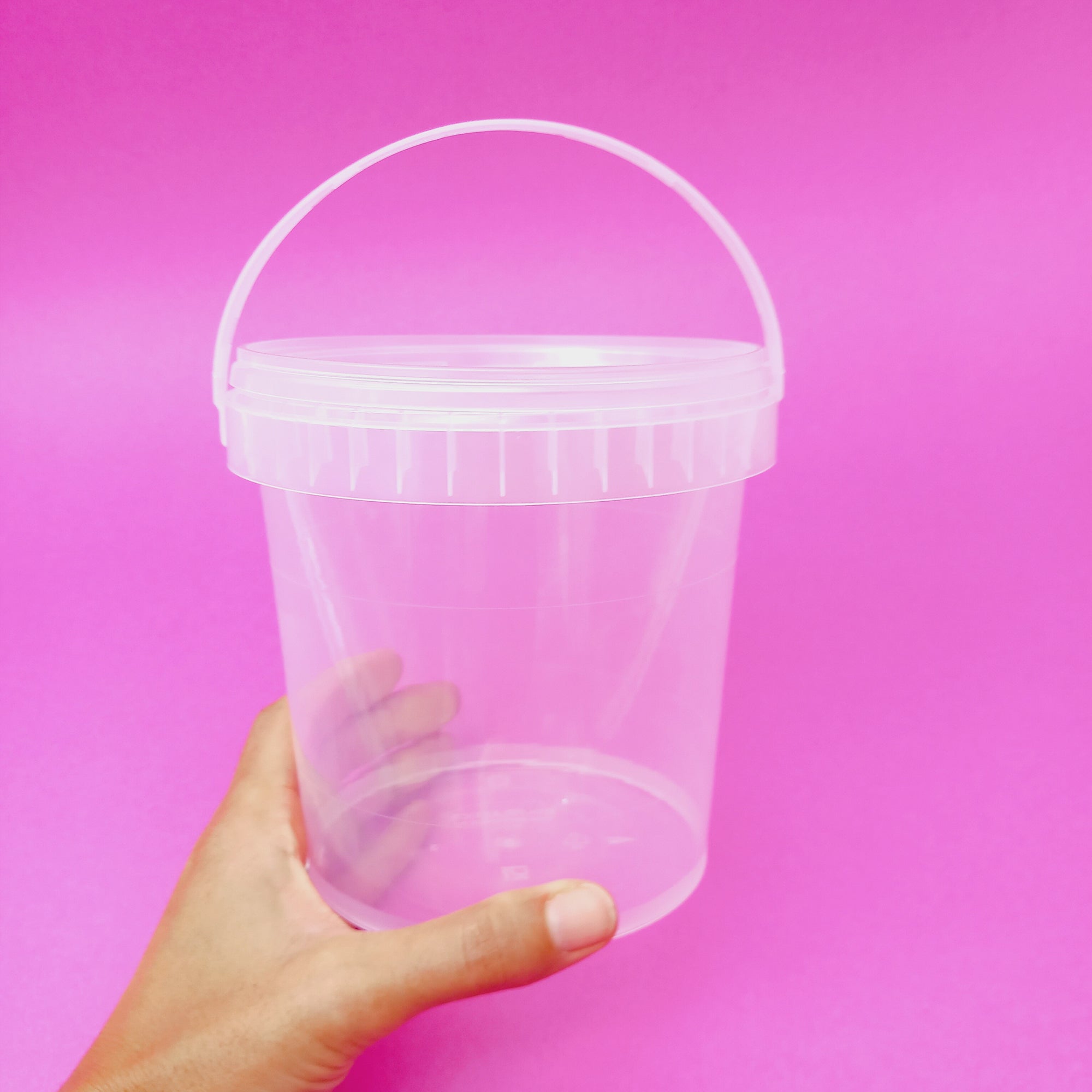 Secchiello trasparente con coperchio su sfondo rosa, retto da una mano