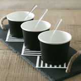 Vaschetta per gelato in cartoncino, nera. Tre disposte vuote su vassoio di ardesia. Cucchiaino di plastica dentro