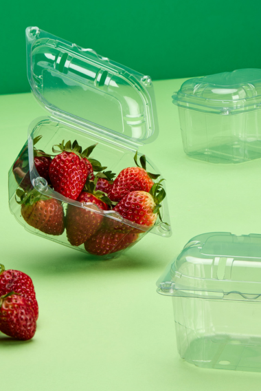 Vaschetta frutta trasparente con coperchio, piena di fragole accanto ad alcune chiuse e vuote