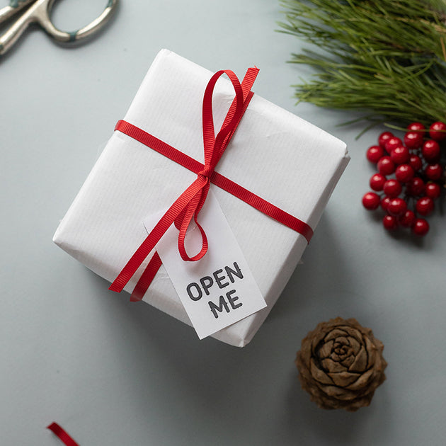 Pacco avvolto da carta bianca e fiocco rosso con cartellino open me