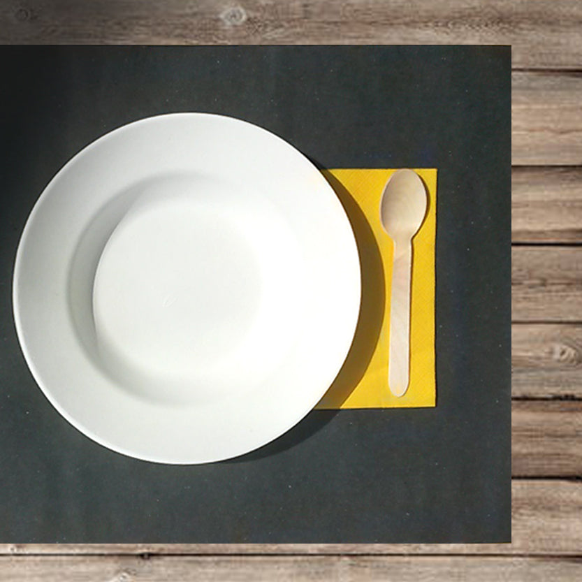 Tovaglietta carta paglia nera con tovagliolo di carta giallo, cucchiaio di legno e piatto bianco