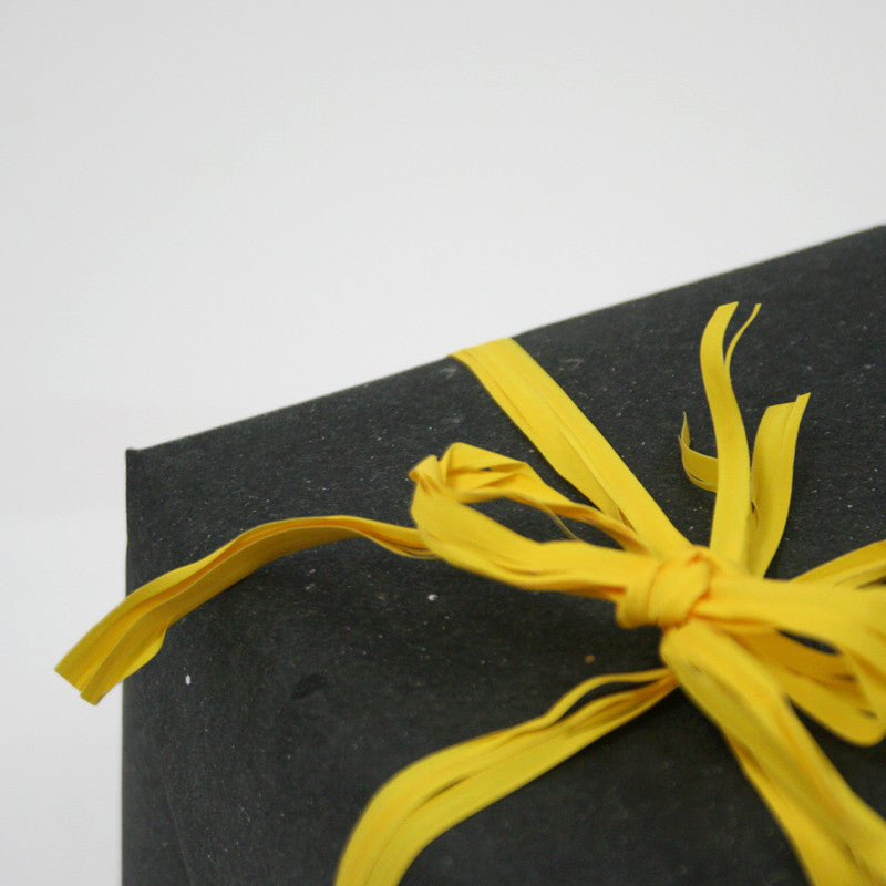 Dettaglio di pacco chiuso con carta nera e fiocco giallo