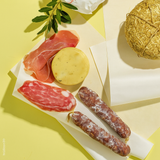 Tavola gialla con carta alimentare, prosciutto, salumi e formaggi 