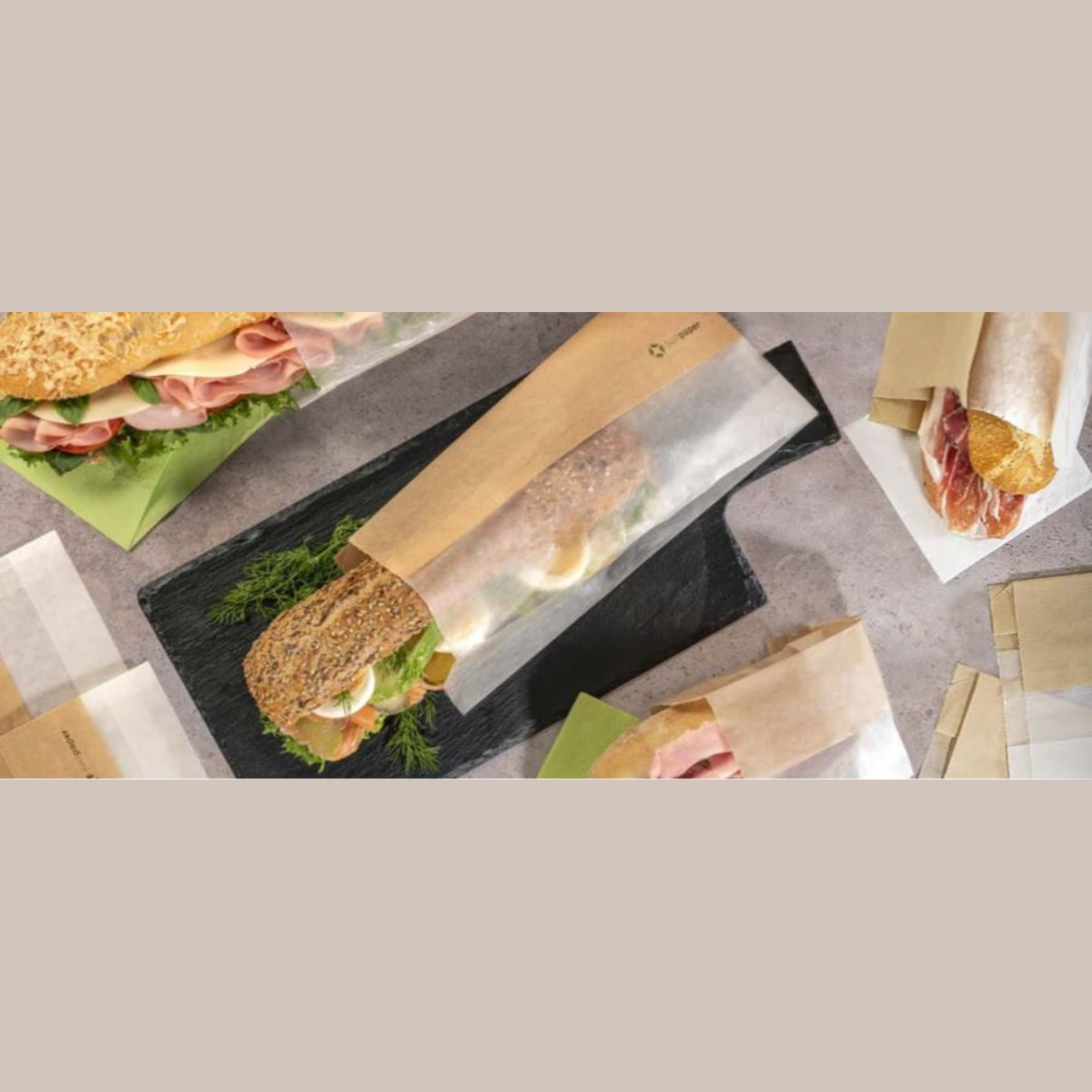 sacchetto color avana con finestra con dentro un panino, su un tavolo pieno di panini