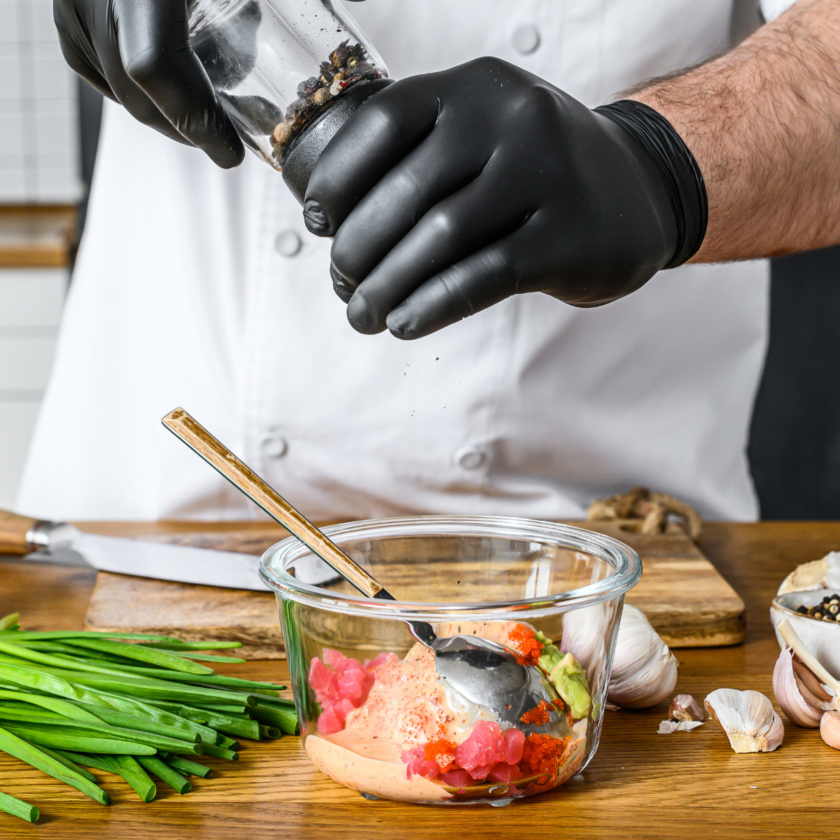Chef che condisce una preparazione indossando guanti neri 