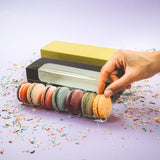 Confezioni di macarons, una trasparente, una nera con finestra ed una verde, ed una mano 