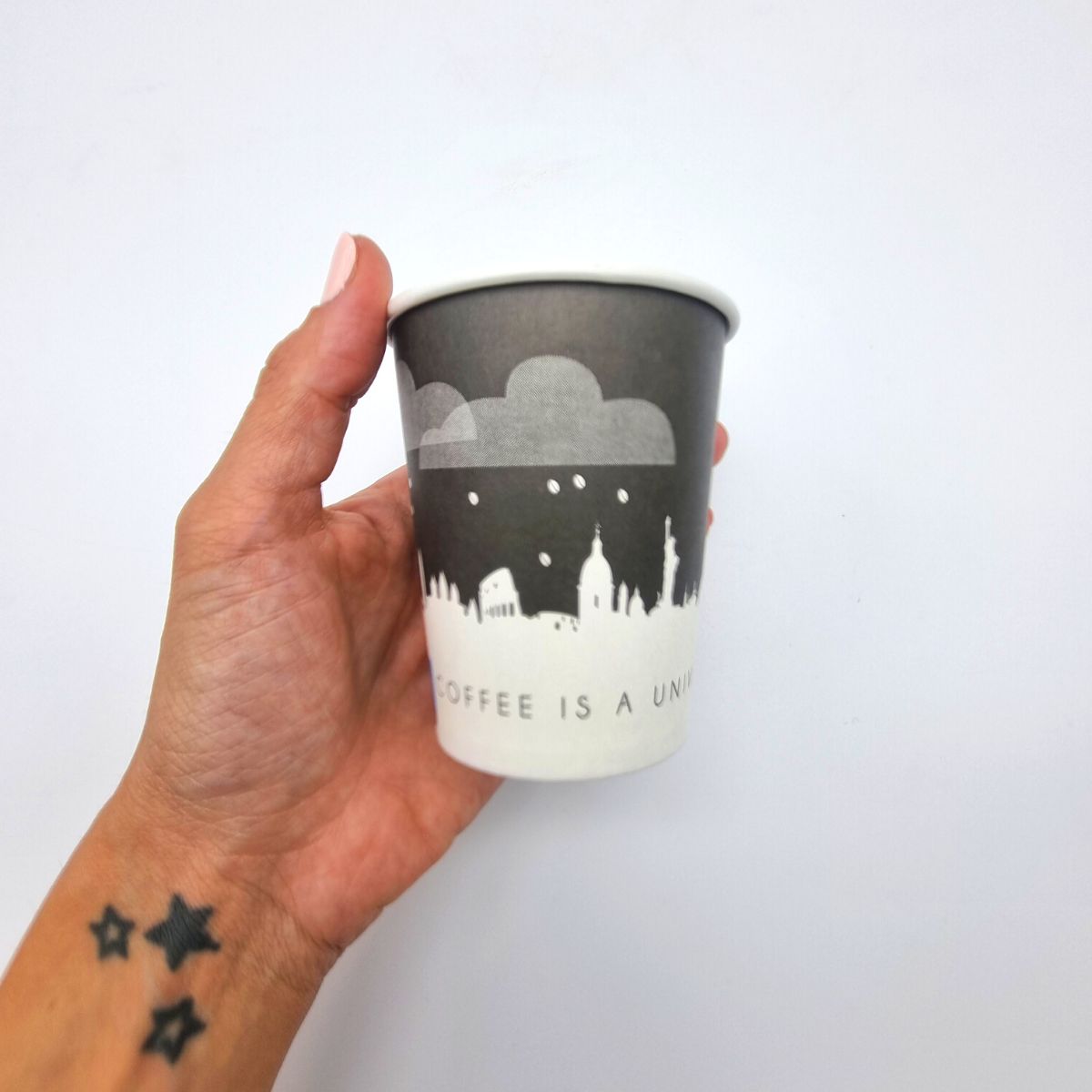 Mano che regge bicchiere monouso  di carta con skyline di citta famose