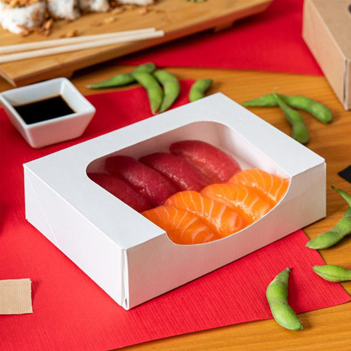 Scatola bianca in cartone con finestra piena di sashimi su una tavola con elementi della cucina giapponese 