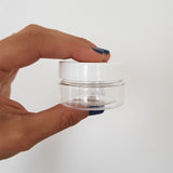Mano che regge vasetto tondo basso trasparente con tappo bianco