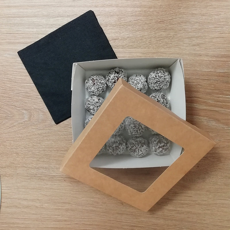 Vaschetta di cartone piena di bon bon al cocco vista da sopra con coperchio appoggiato e fazzoletto di carta nero