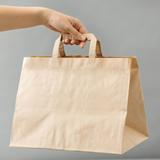 Mano che regge una shopper di carta color avana a fondo largo 