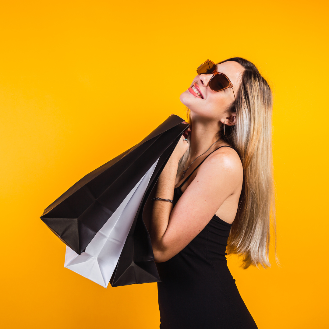 Ragazza con occhiali da sole, bionda, sorridente, che tiene due shopper 