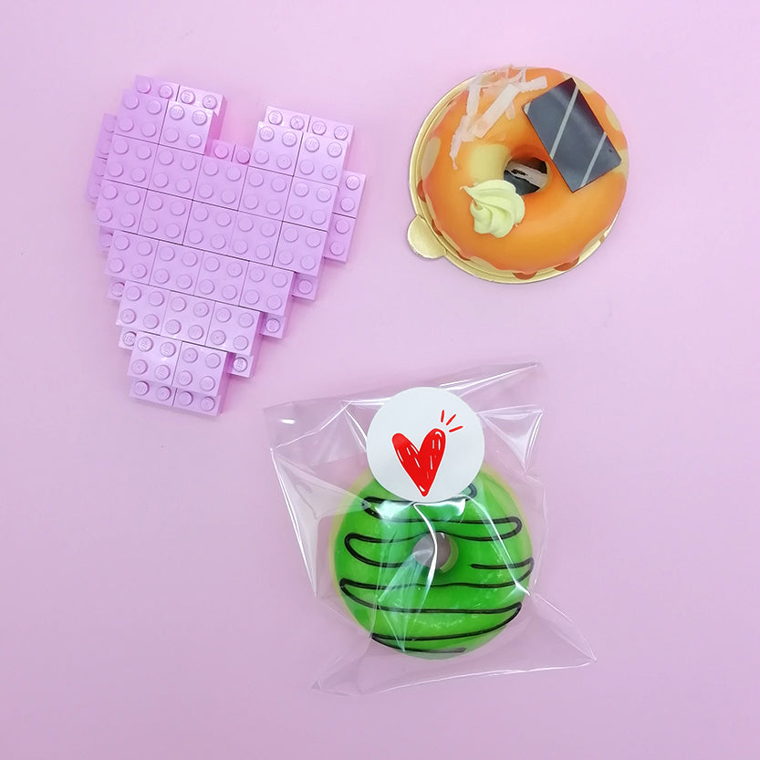 Busta trasparente sigillata con etichetta tonda personalizzata , donuts su piattino monoporzione dorato e cuore lego viola 