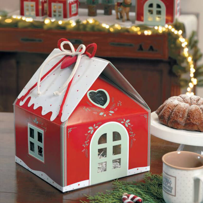 Casetta rossa porta panettone su tavolino di legno con decori ed elementi natalizi