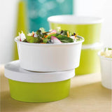 Contenitori per cibo d'asporto, bianchi e verdi, tondi, impilati su tavolo con  dell'insalata