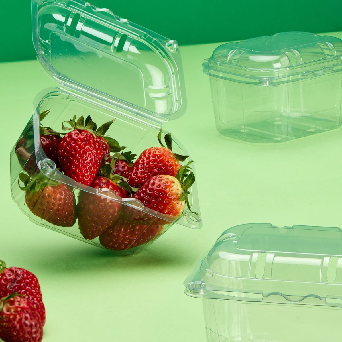 Vaschette per frutta e verdura con coperchio unito in materiale R-PET. Die vuote, una ripiena di fragole. Su sfondo verde