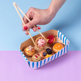 Mano che con delle bacchette prende un pasticcino dentro un vassoio di carta color bianco e blu 