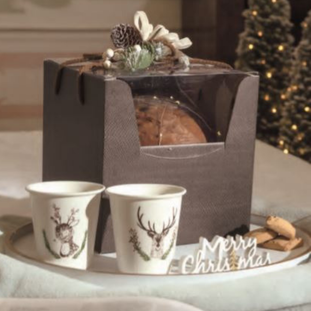 Scatola con finestra porta panettone, con panettone dentro, su vassoio con bicchieri ed elementi natalizi
