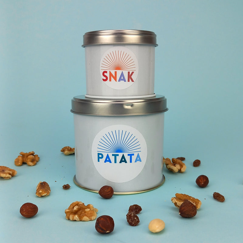 Due barattolini di latta, due misure diversi, tondi, uno sull'altro, uno con etichetta patata ed uno etichettato snack