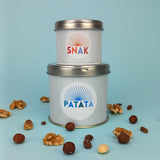 Due barattolini di latta, due misure diversi, tondi, uno sull'altro, uno con etichetta patata ed uno etichettato snack