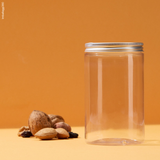Barattolo trasparente con tappo di alluminio, chiuso. vuoto, accanto a frutta secca su sfondo arancione