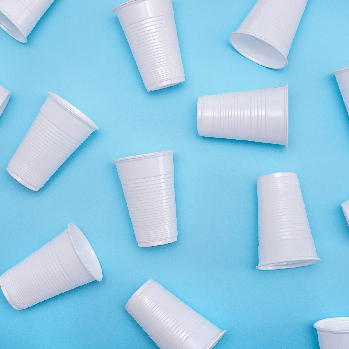 Bicchieri di plastica monouso bianchi sparsi su sfondo azzurro