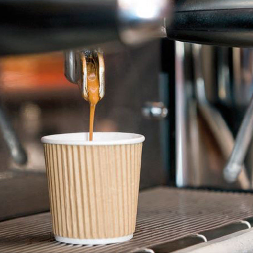 Bicchierino per caffe da asporto di carta color avana, ondulato, in una macchina per il caffe da bar, nell'atto di essere riempito 