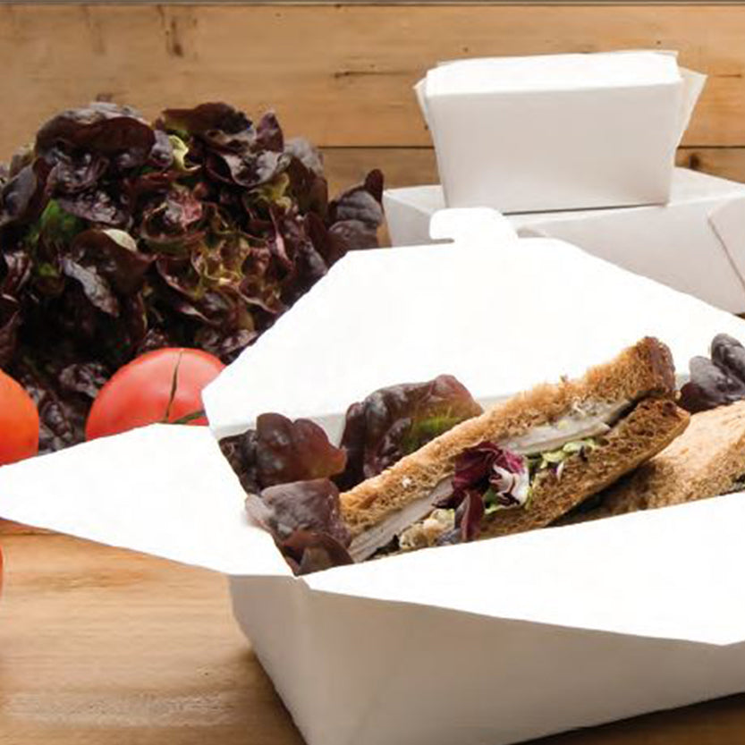 Scatola per alimenti, bianca, aperta, contenente insalata e due panini. Sullo sfondo due scatole ma chiuse e della verdura