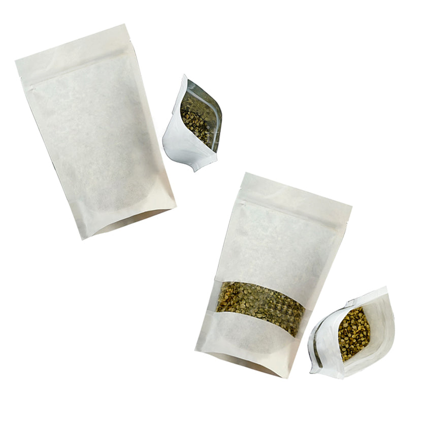 Busta bianca con zip e finestra, piena di semi, vista sdraiata da sopra aperta. Due diverse misure