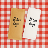 Buste porta posate personalizzate con il tuo logo. Una color avana, una bianca, su tovaglia a quadretti bianco e rossi