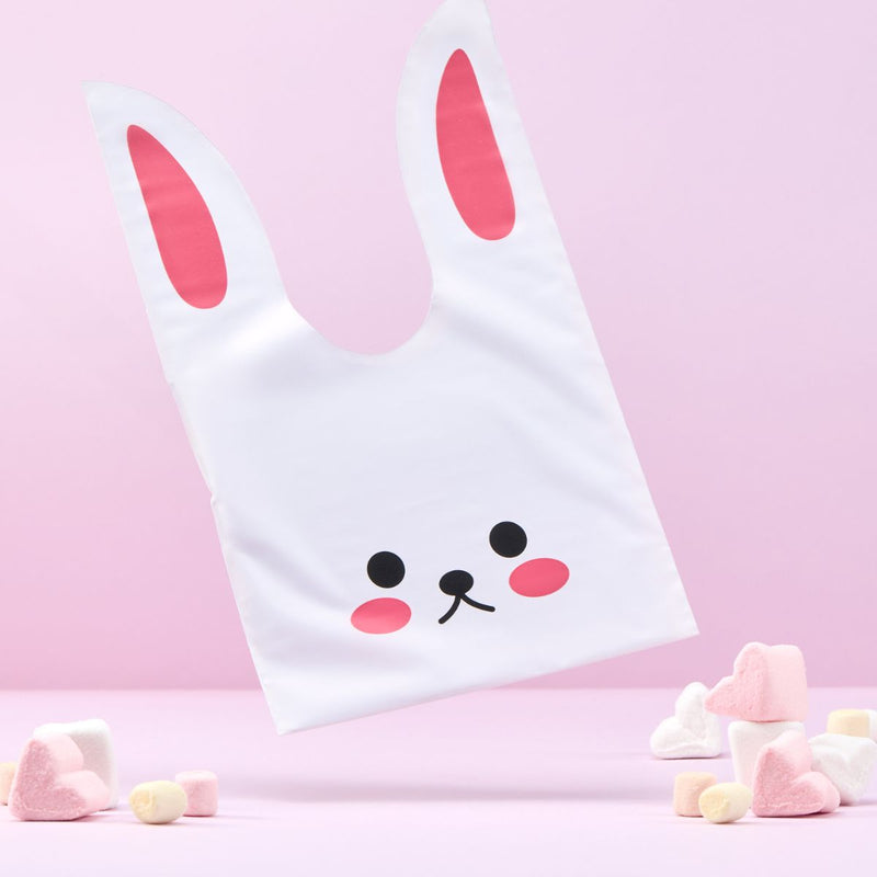 Busta per regalo pasquale a forma di coniglio, caramelle vicino e sfondo rosa 
