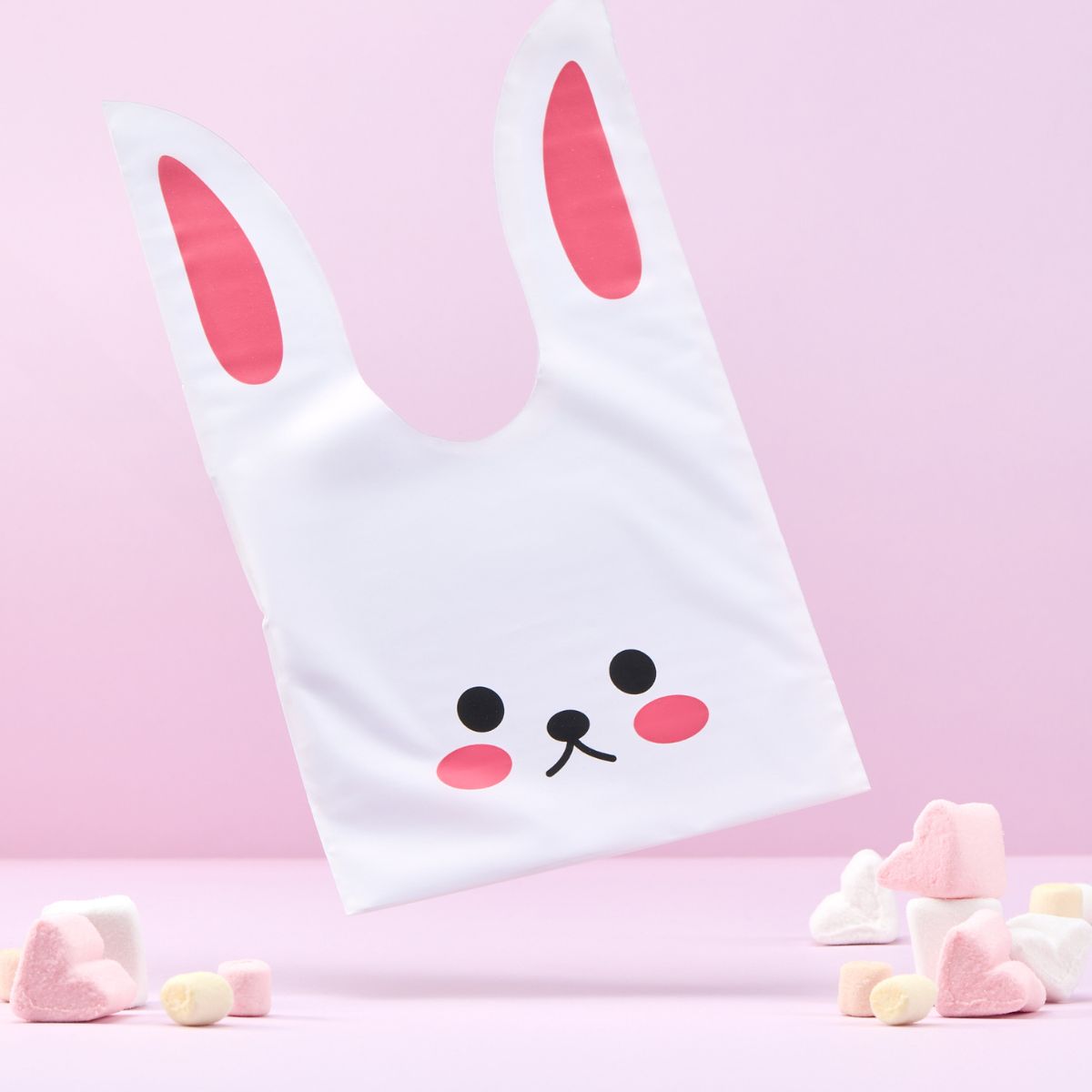 Busta per regalo pasquale a forma di coniglio, caramelle vicino e sfondo rosa 