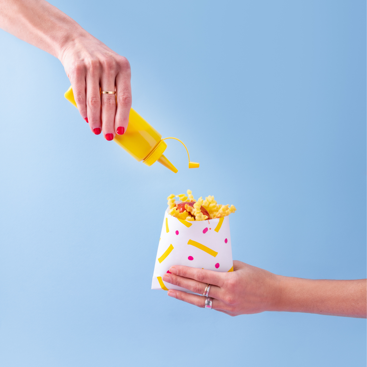 Mani che reggono patatine fritte in una busta di carta nell'atto di versarci maionese 