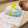 Carta colomba bianca con scritte color tiffany di buona Pasqua attorno ad una colomba e nastro giallo , su carta con scritte arancioni, su un tavolino accanto ad una colomba