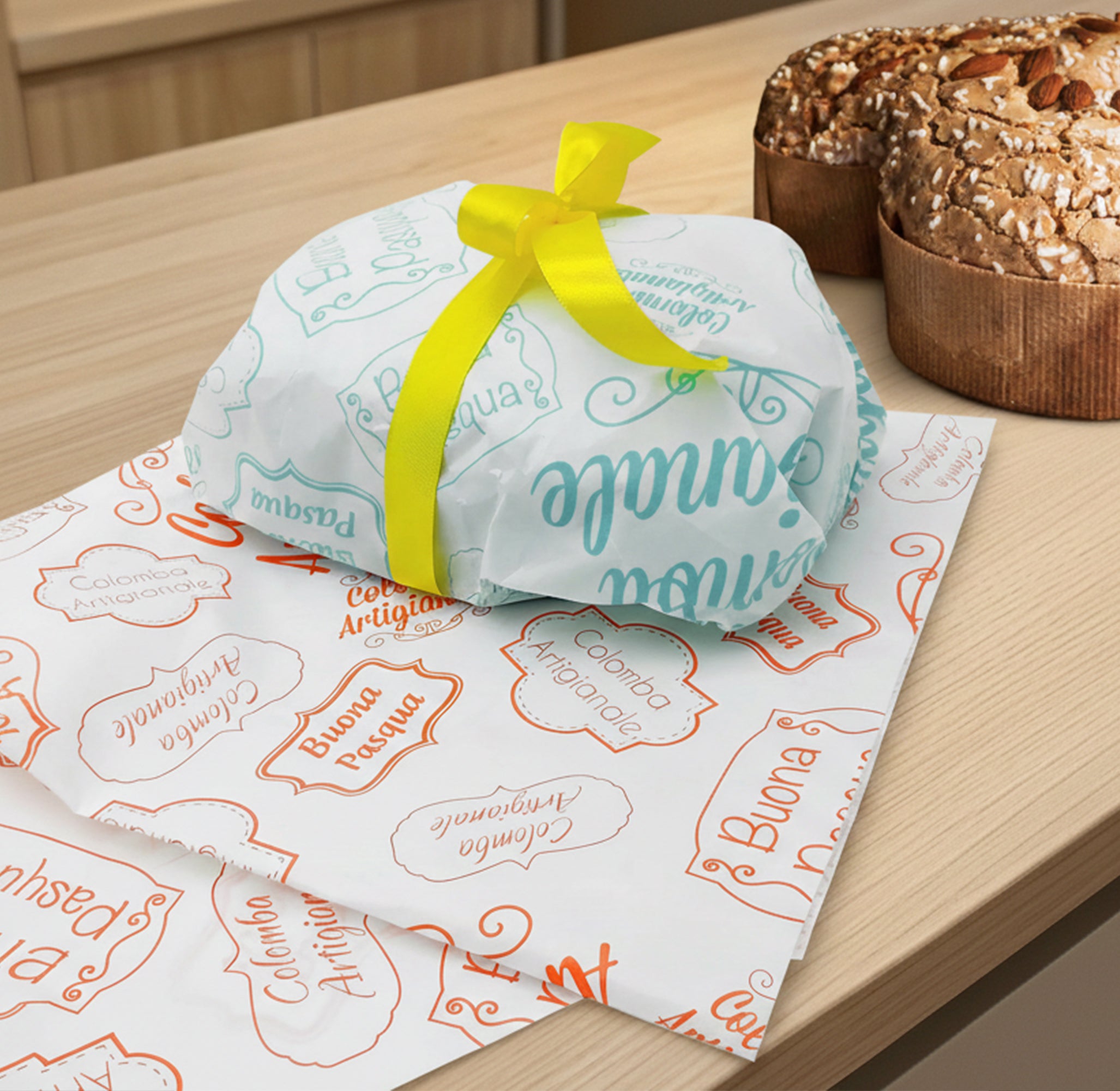 Carta colomba bianca con scritte color tiffany di buona Pasqua attorno ad una colomba e nastro giallo , su carta con scritte arancioni, su un tavolino accanto ad una colomba