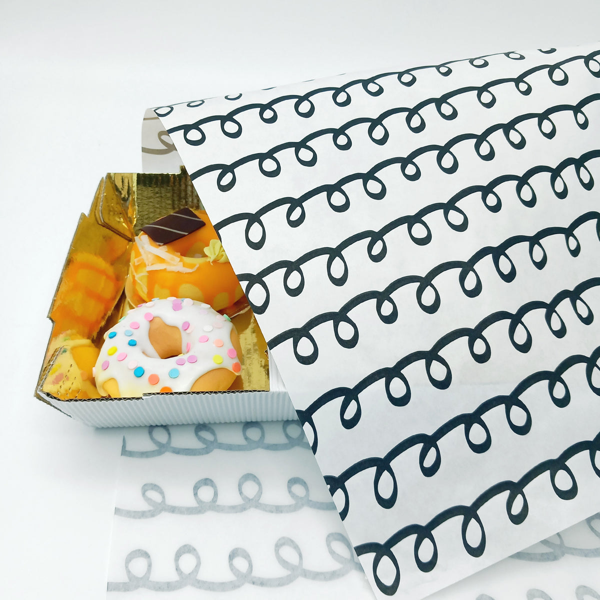 Carta per pasticceria a riccioli neri che avvolge un vassoio di paste