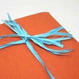 Dettaglio di pacco chiuso con carta paglia rossa e nastro di rafia azzurro