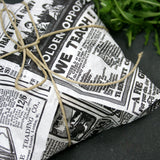 Dettaglio pacco chiuso con carta alimentare bianca con scritte nere e spago su tavolo nero vicino a della rucola