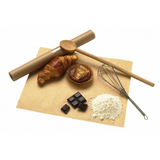 Carta da  forno stesa con sopra_ mattarello, cornetto, brioches, scacchi di cioccolato, una frusta, mestolo di legno e un po di farina 