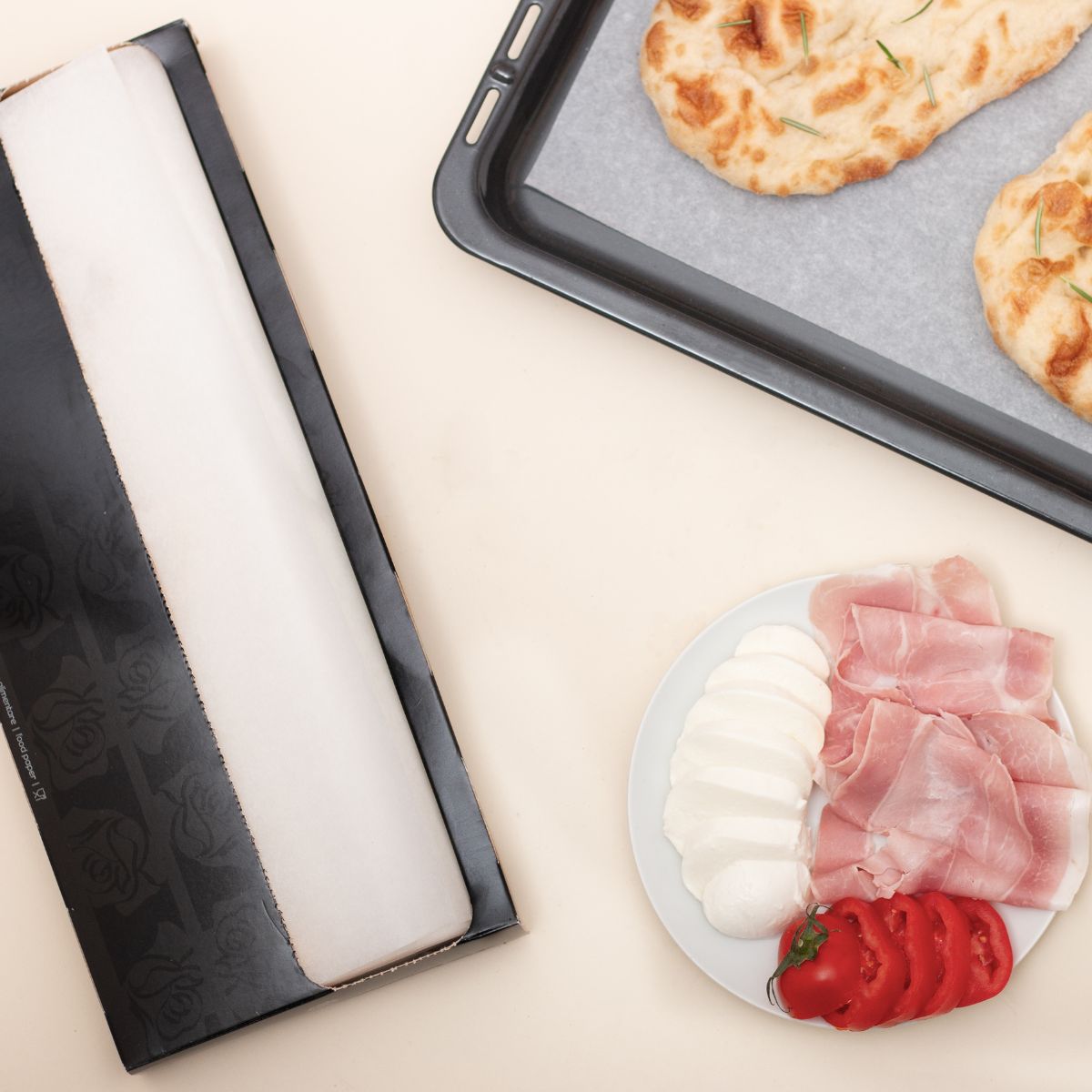 Carta forno nel suo box, accanto ad una teglia ed un  piatto con affettati e formaggio