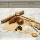Tavola da lavoro con sopra carta paglia, scacchi di cioccolato, attrezzi da cucina, ella farina e dei dolci 