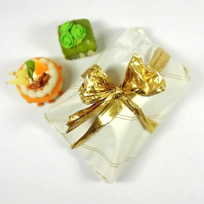Vassoio di paste incartato da carta bianca con fiocco metallizzato oro